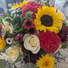 Mixed bouquet with yellow sunflowers, ivory roses, red textured blooms and small daisies in a tight arrangement