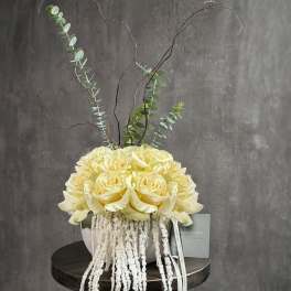 Cream rose arrangement in a round vase with tall eucalyptus branches