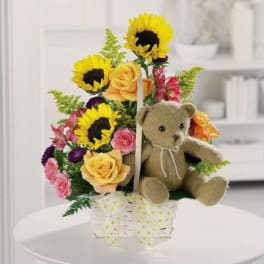 Sunflower and rose arrangement with a teddy bear in a clear basket