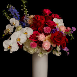 Mixed bouquet of red roses, white orchids, and blue flowers in a white vase
