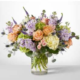 Bouquet of peach roses, lavender blooms, and hydrangeas in a clear glass vase