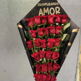 Tall bouquet of red roses arranged in rows in black wrap with gold lettering and a red bow