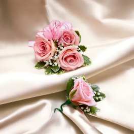 Two pink rose boutonnieres with ribbon accents on satin fabric