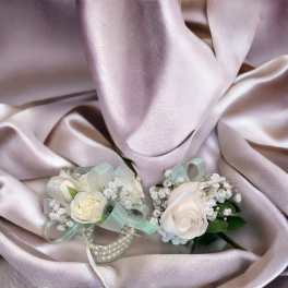 Two white rose corsages with ribbon and pearl accents on satin fabric