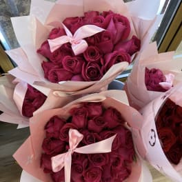 Bouquets of deep pink roses wrapped in pale pink paper with satin bows