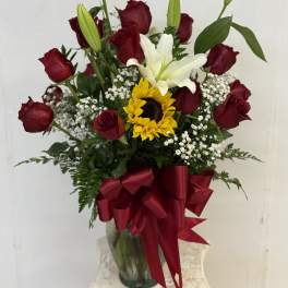 Bouquet of red roses, a white lily, and a sunflower in a glass vase