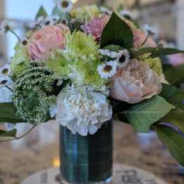 Pastel bouquet of pink roses, white carnations, green mums and small daisies in a clear glass vase