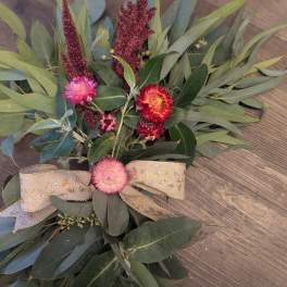 Rustic greenery swag with pink and red flowers and a gold patterned ribbon bow