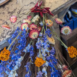 Rustic twig broom decorated with dried blue, orange, and cream flowers and red peppers.