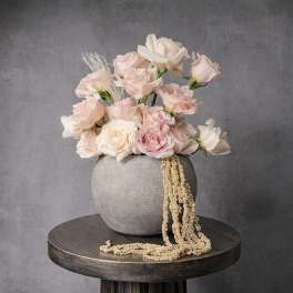 Low arrangement of blush and ivory roses in a round gray vase with cascading dried accents.