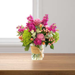 Pink roses and magenta flowers in a glass vase with burlap ribbon
