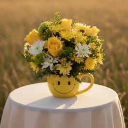 Yellow and white flower arrangement in a smiley-face mug