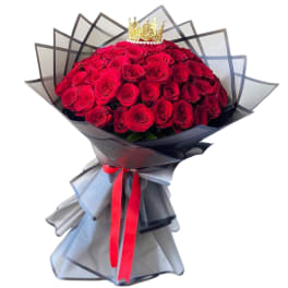 Large bouquet of red roses wrapped in black paper with a crown topper