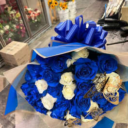 Bouquet of vivid blue and white roses wrapped in blue paper with a large bow.