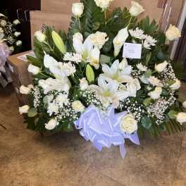 Large white sympathy arrangement with lilies and roses accented by a big white bow.