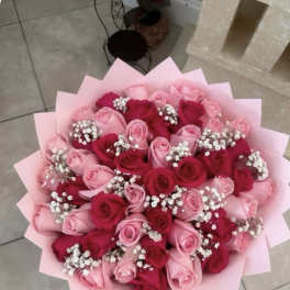 Round bouquet of pink and red roses with white filler flowers wrapped in pink paper