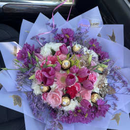 Round bouquet of pink and purple flowers with chocolates in lavender wrapping paper