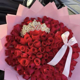 Large bouquet of tightly packed red roses with jeweled tiara, wrapped in pink paper with white ribbon