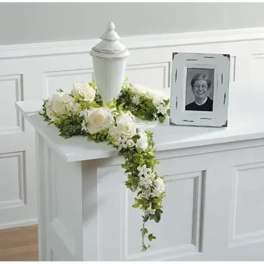 White floral casket spray with a trailing greenery garland and urn centerpiece