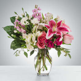 Pink lilies, roses, and white blooms arranged in a clear glass vase