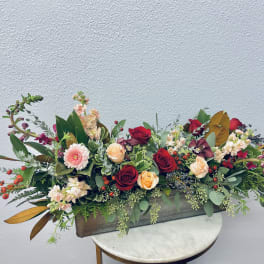 Long floral centerpiece with red and peach roses in a rectangular container