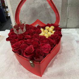 Red roses arranged in a heart-shaped gift box with gold chocolates and a jeweled crown