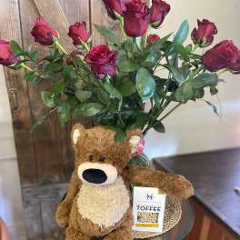 Red rose bouquet in a vase with a brown teddy bear and box of toffee candy