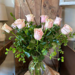 Tall arrangement of light pink roses with abundant foliage in a clear glass vase