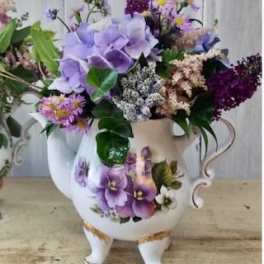 Purple floral arrangement in a white ceramic pitcher vase