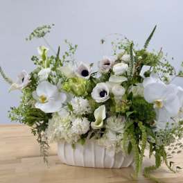 Low white arrangement with orchids, anemones, calla lilies, and hydrangeas in a white ceramic vase
