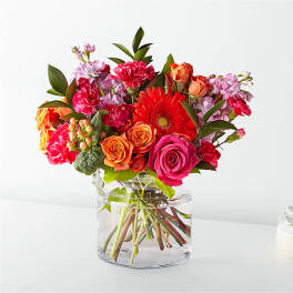 Mixed bouquet of roses, gerbera daisies, and carnations in a clear glass vase