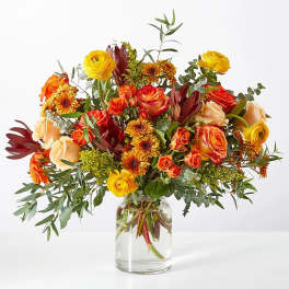 Mixed bouquet of orange and yellow flowers in a clear glass vase