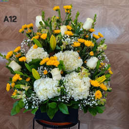 Large floral arrangement with white roses, hydrangeas, and yellow daisies in a black container