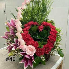 Tall floral arrangement with pink roses, lilies, and red carnations in a basket