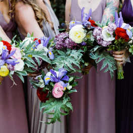 Bridesmaids holding colorful bouquets with purple, pink, white, and red flowers