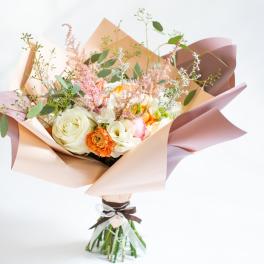 Bouquet of cream, peach, and pink flowers wrapped in pastel paper