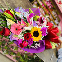 Colorful bouquet with roses, lilies, gerbera daisies, and a sunflower wrapped in purple paper
