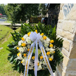Standing wreath of yellow roses and white flowers with a white bow on an easel