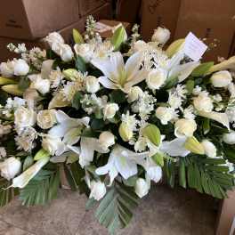 Long, low arrangement of white lilies and roses with other white blooms and large palm leaves.
