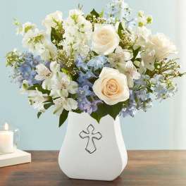 White and pale blue flower arrangement in a white vase with a cross emblem