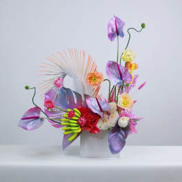 Colorful floral arrangement in a white square vase with purple anthuriums