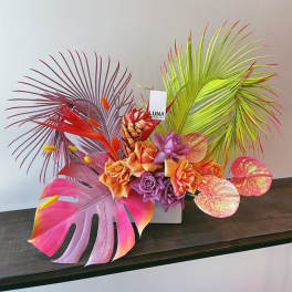 Tropical floral arrangement with orange and purple roses and colorful palm leaves