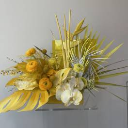 Yellow floral arrangement with orchids and tropical leaves in a rectangular container