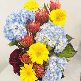 Bouquet of blue hydrangeas, yellow gerberas, and red pincushion flowers in a vase