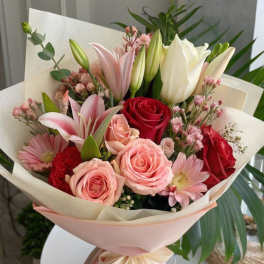 Bouquet of pink and red roses with lilies and daisies wrapped in pale paper