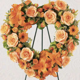 Heart-shaped floral wreath with orange roses and lilies on a stand