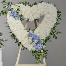 Heart-shaped white floral wreath with blue accents on a wooden easel