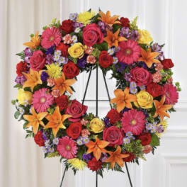 Heart-shaped floral wreath on a stand with roses, lilies, and daisies