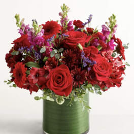 Red roses and mixed flowers arranged in a green glass vase
