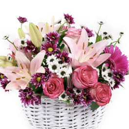 Basket of pink lilies, roses, and mixed daisies arranged in a white woven container